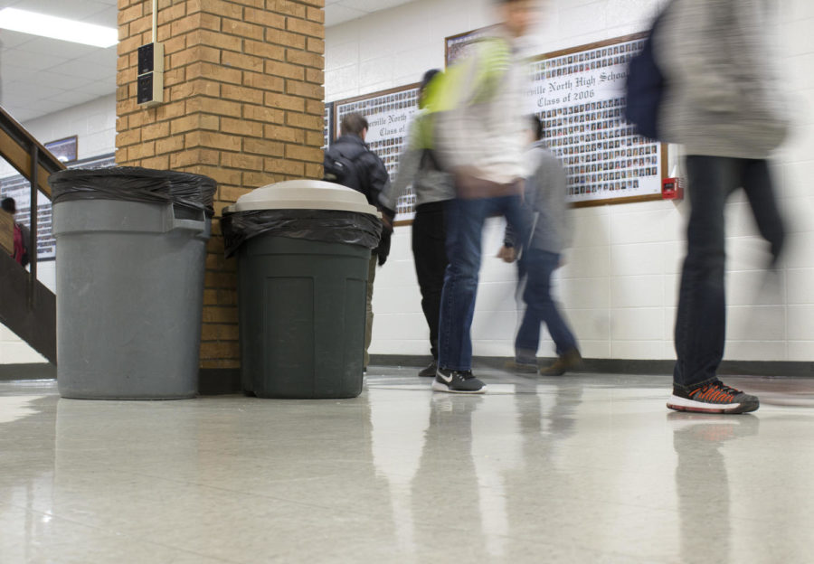 Students walk through the hallway during their passing period. Recycling bins are scattered around the school and can be identified by their beige-colored lids or their blue color and a Recycling “Mobius” symbol.