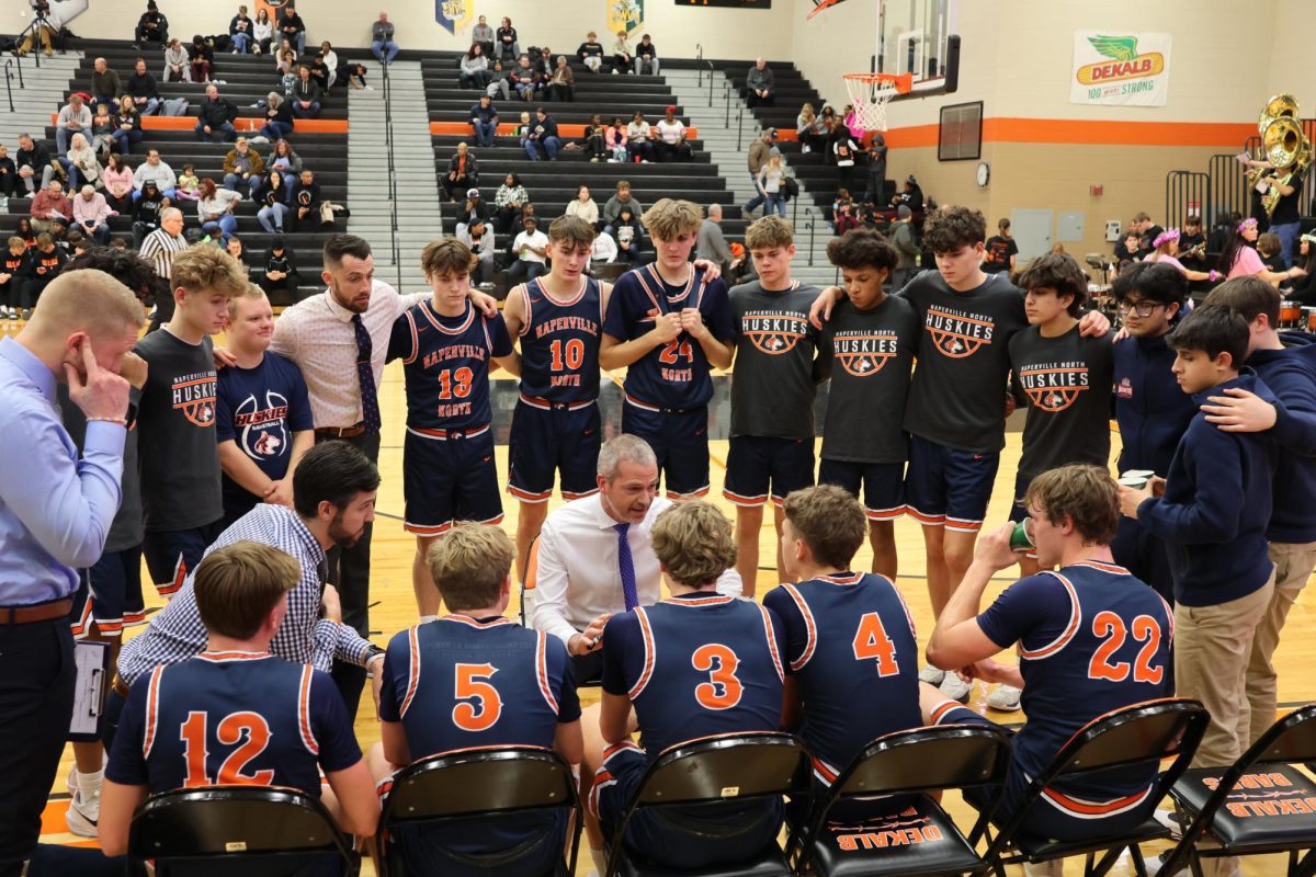 The Naperville North varsity boys basketball team listens closely to Head Coach Gene Nolan at a previous match from this season.