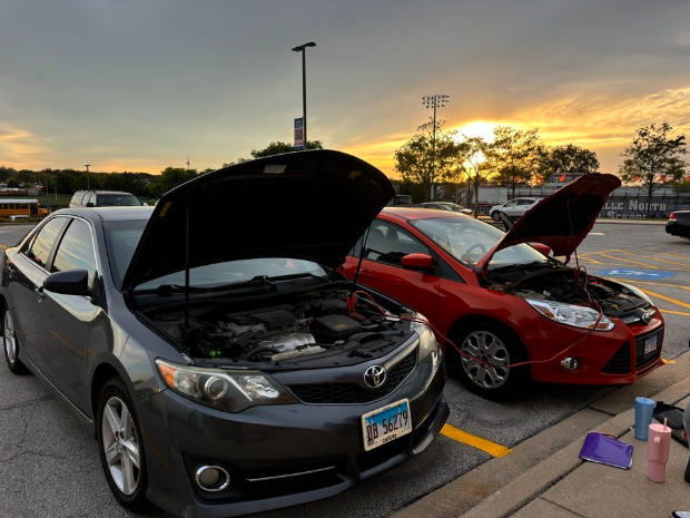 Two cars are hooked up to be jump-started in an NNHS parking lot.