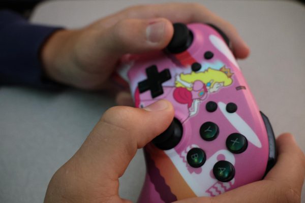 A person holding a HORI brand Nintendo Switch Pro Controller with the character Princess Peach on it.